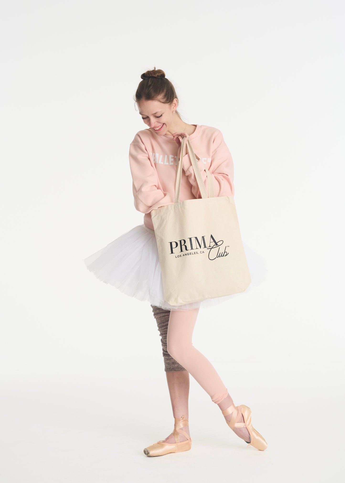 model looking inside canvas tote bag with Black Prima Club logo on outside
