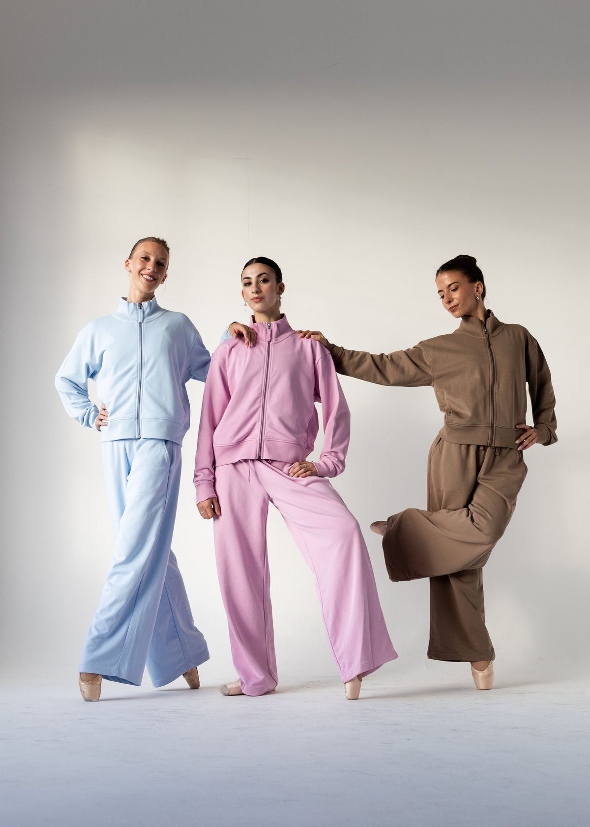 Three models wearing matching lounge sets in light blue, pink, and brown, posed together against a neutral studio background.